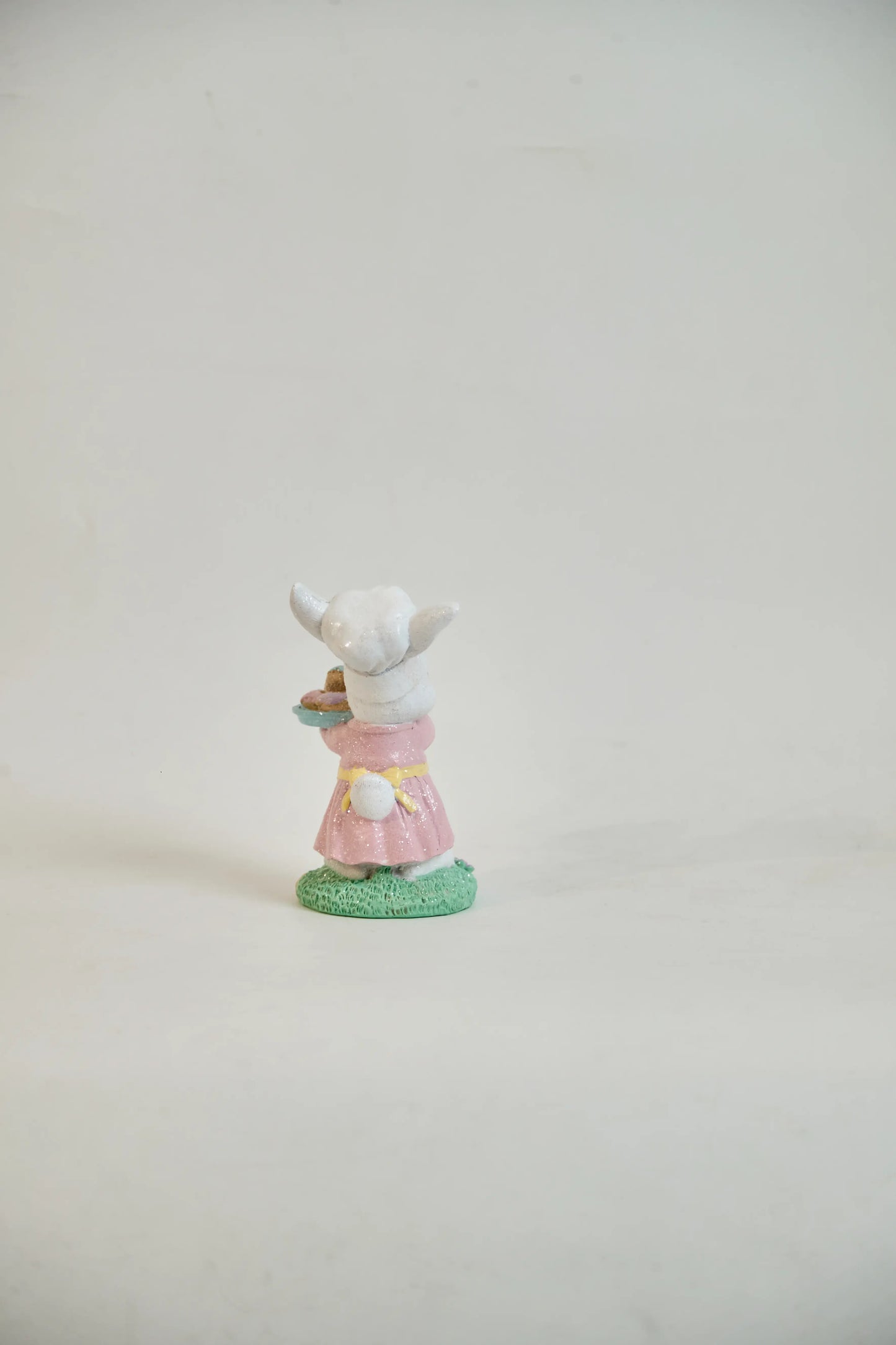 Rear view of Easter bunny figurine showing white cotton tail, yellow sash, and pink ruffled hem — glitter resin spring tabletop accent