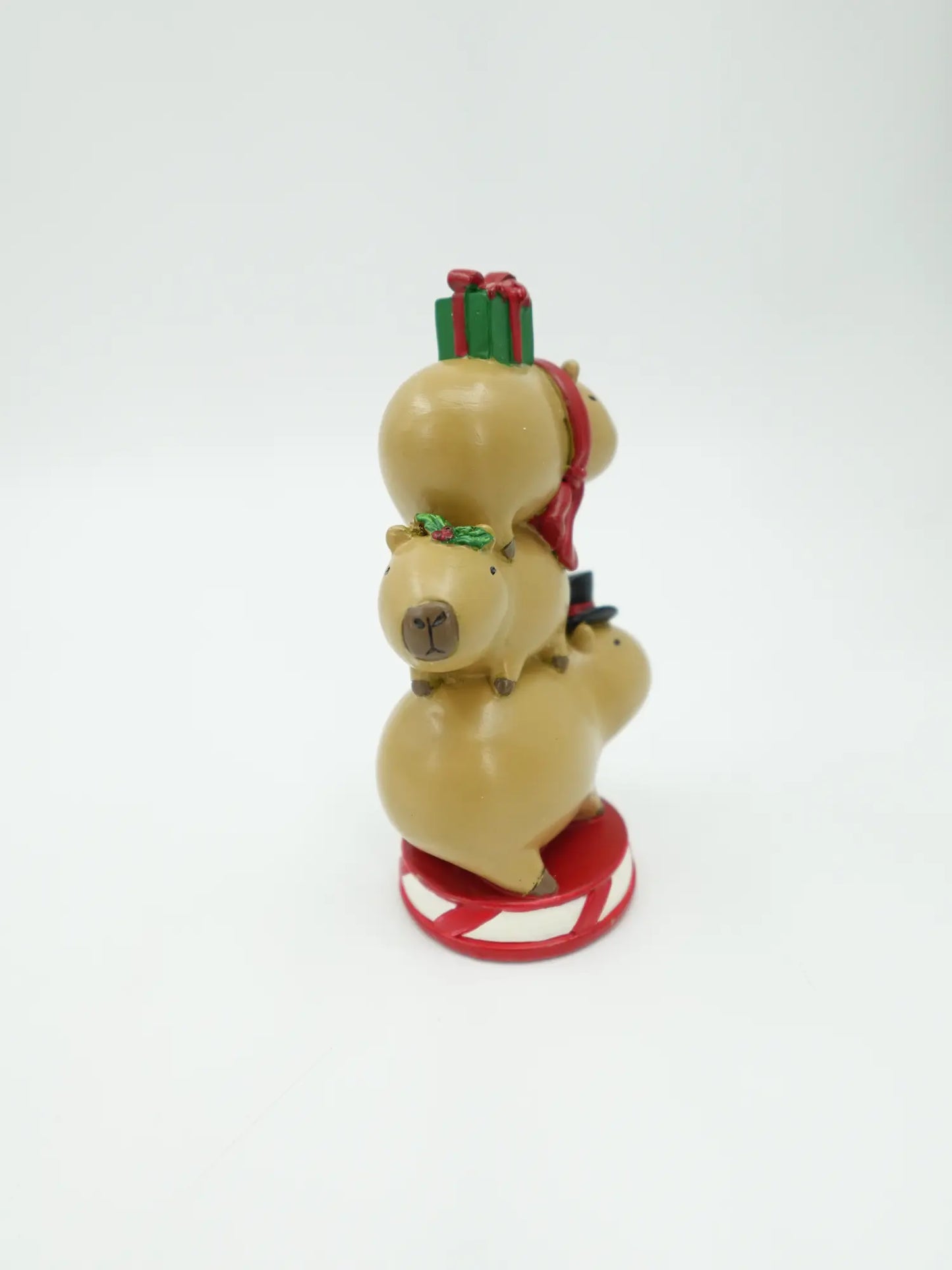 three stacked capybaras figurines showing the vertical totem silhouette and candy-cane striped circular base