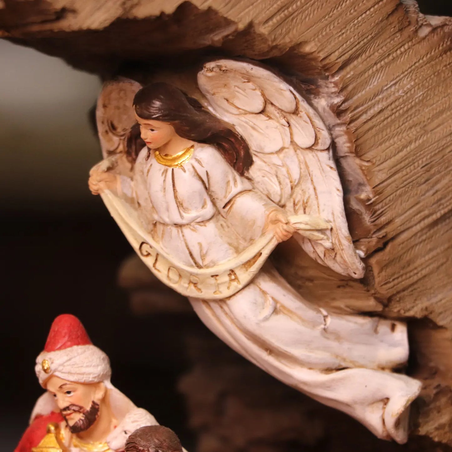 White angel figurine with wings overlooking Christmas nativity scene inside rustic stable