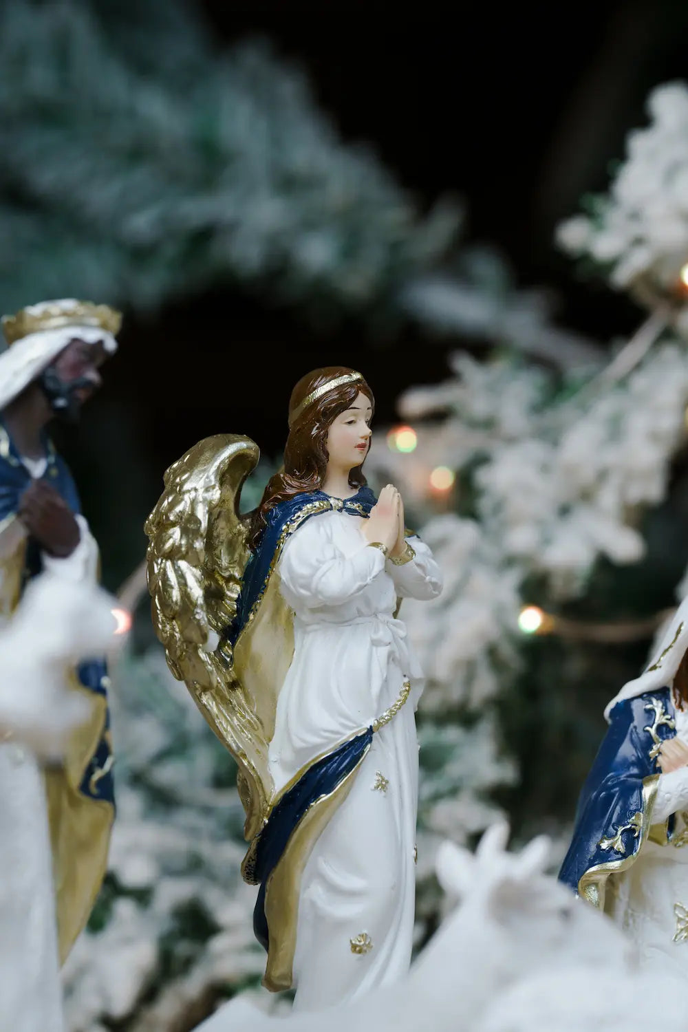 white angel figurine with gold wings and blue trim, standing in a prayer pose.