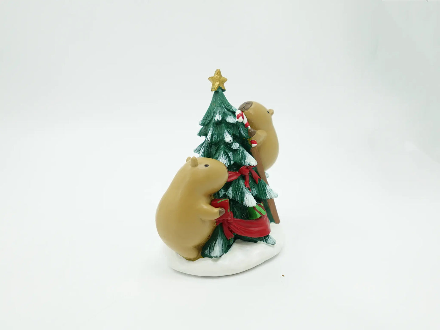 holiday capybara figurines decorating a green Christmas tree with a gold star, red ribbon, and white candy canes, set on a white background.