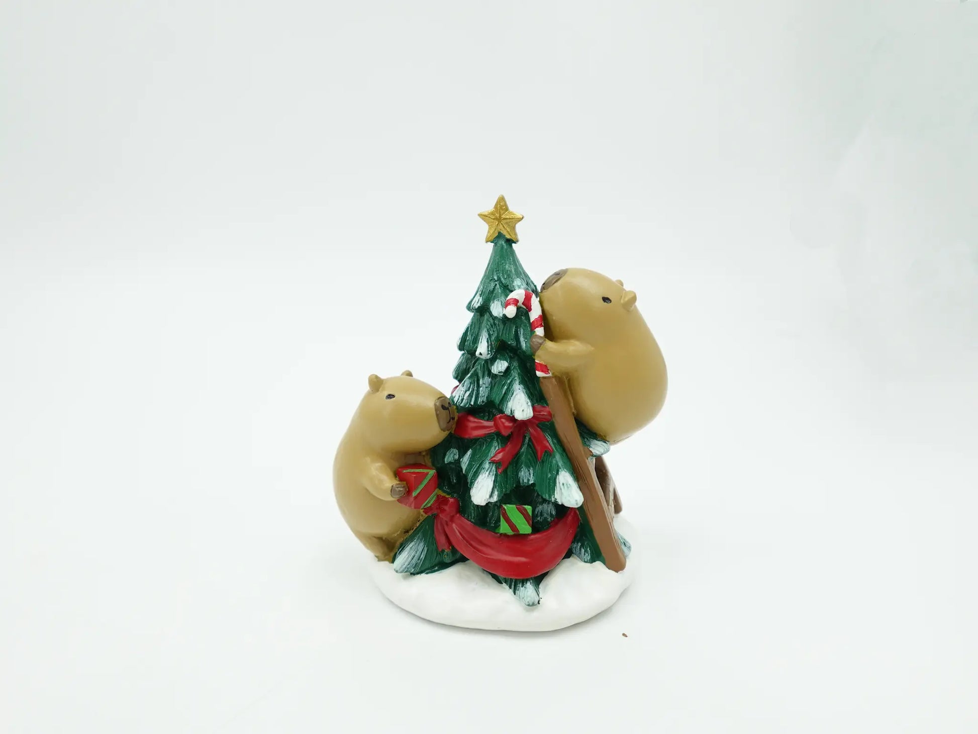 the capybara duo decorating tree figurine showing the tree branches, ribbon details, and snowy base from behind
