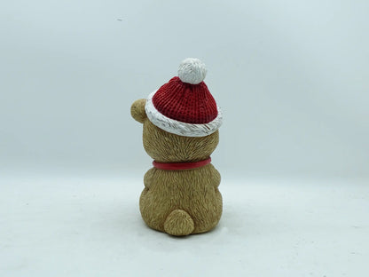the teddy bear figurine showing the textured fur, red collar, and pom-pom hat from behind