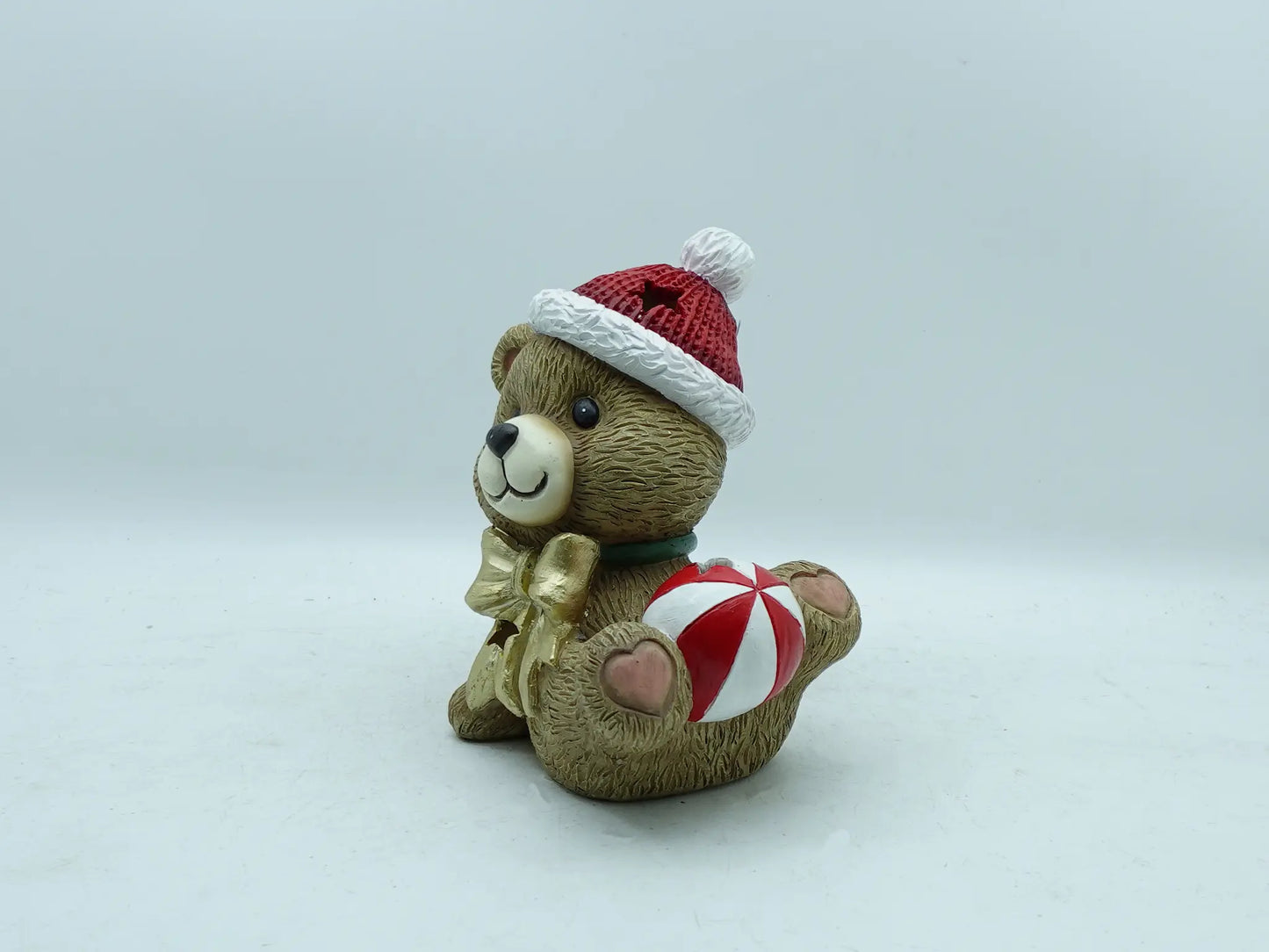 the playful teddy bear figurine lying down, holding the striped Christmas bauble on plain background