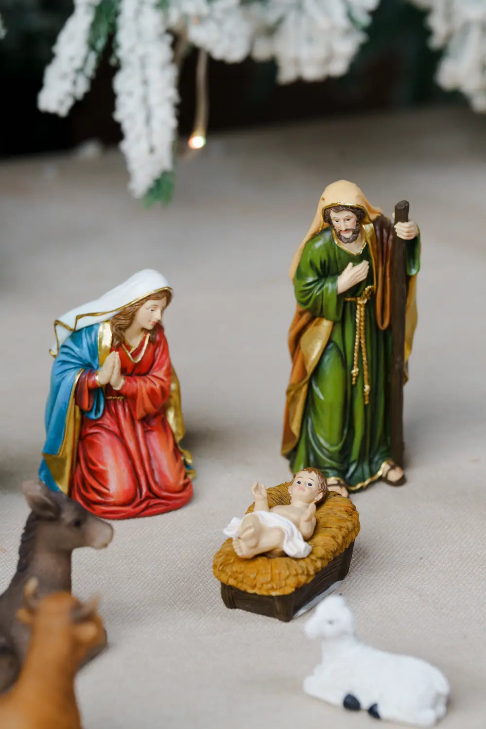 Holy family figurines of Mary, Joseph, baby Jesus in a manger, and small animal figures, arranged on a neutral surface.