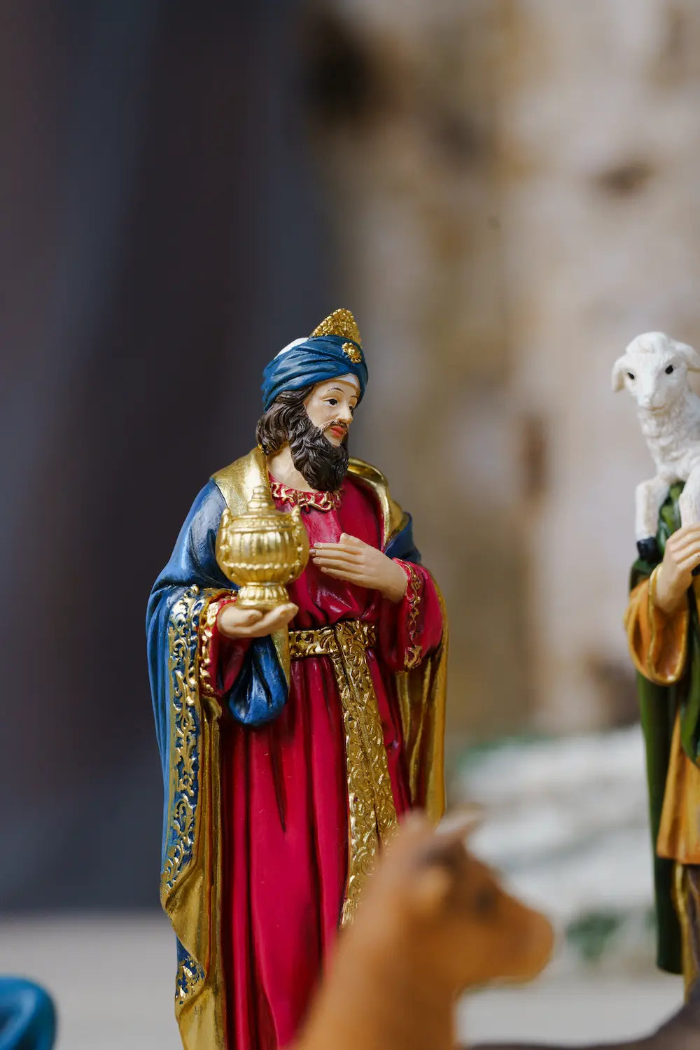 a nativity figurine depicting the Wise Men, with one figure in a red robe and blue turban holding a gold lamp.
