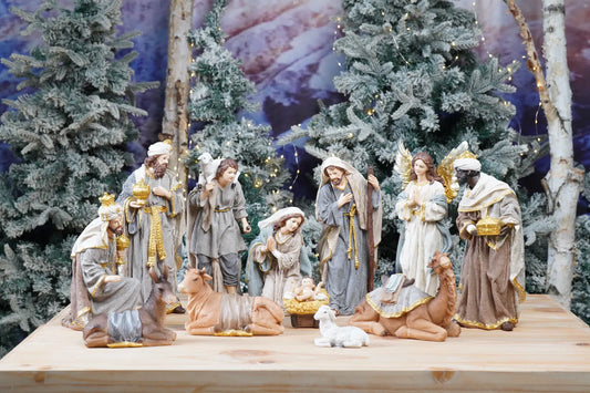 Full 12-piece grey and gold nativity set arranged on pine wood surface with frosted winter tree backdrop