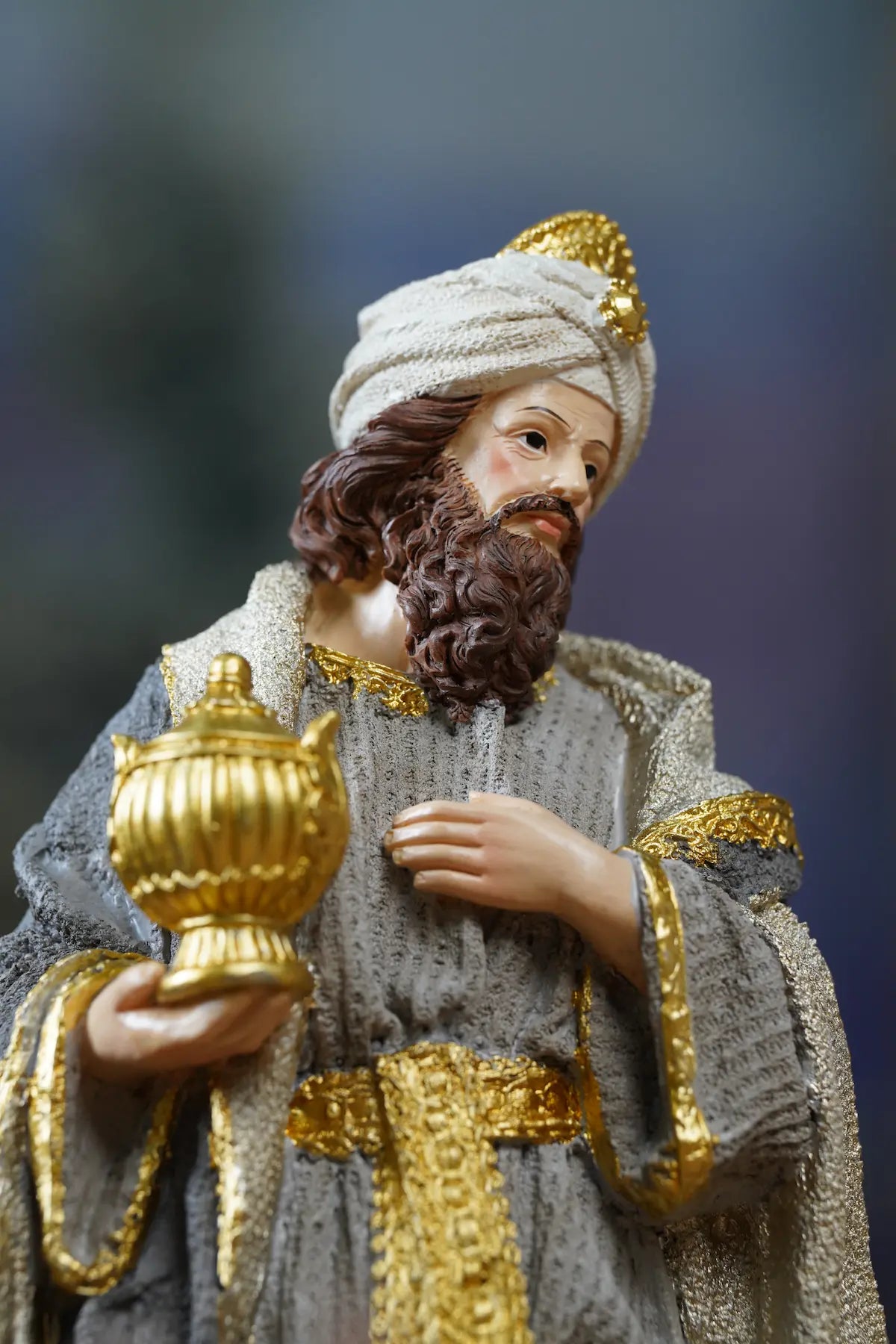 Wise Man nativity figurine close-up — grey textured robe with gold trim holding ornate golden urn gift