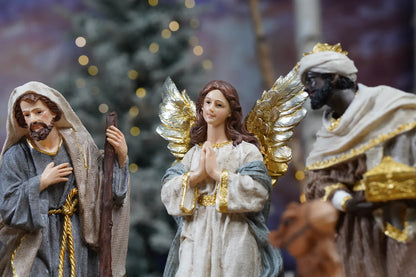 Praying angel and Joseph nativity figurines close-up — angel with gold and silver metallic wings in prayer pose beside Wise Man