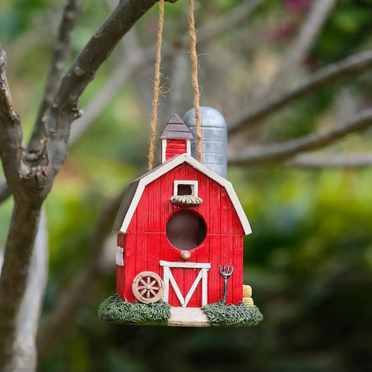 Red barn birdhouse with silo hanging from tree branch outdoors