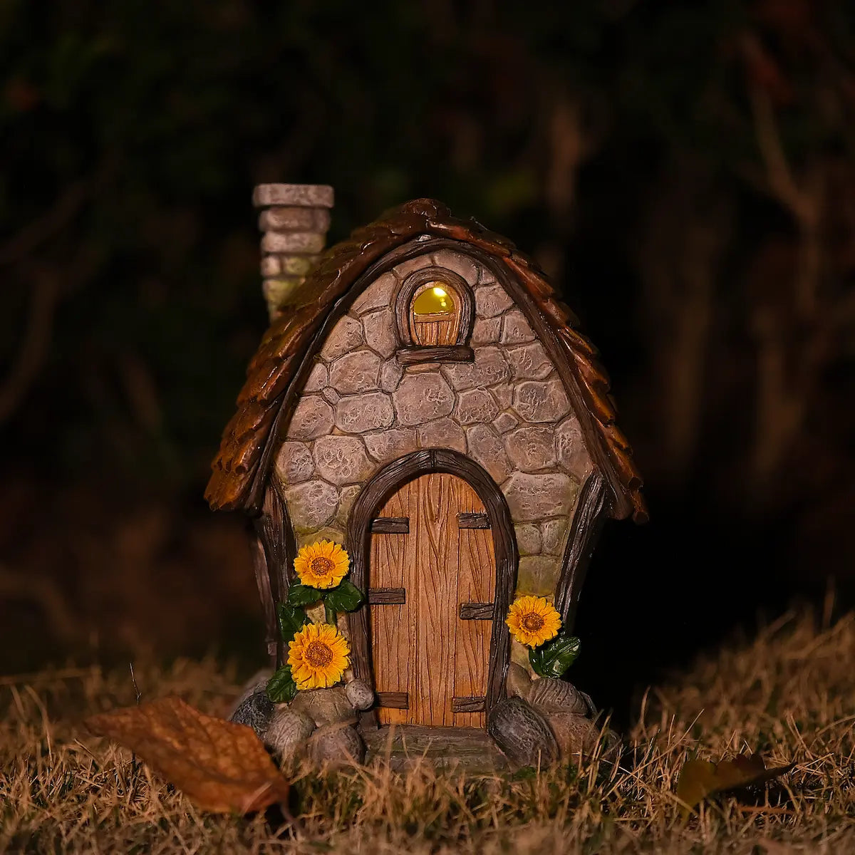 Solar sunflower fairy house glowing warm amber LED light at night in garden grass