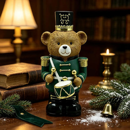 A decorative teddy bear figurine wearing a green uniform and black hat, standing on a wooden surface with holiday greenery, books, a lamp, and a candle in the background.