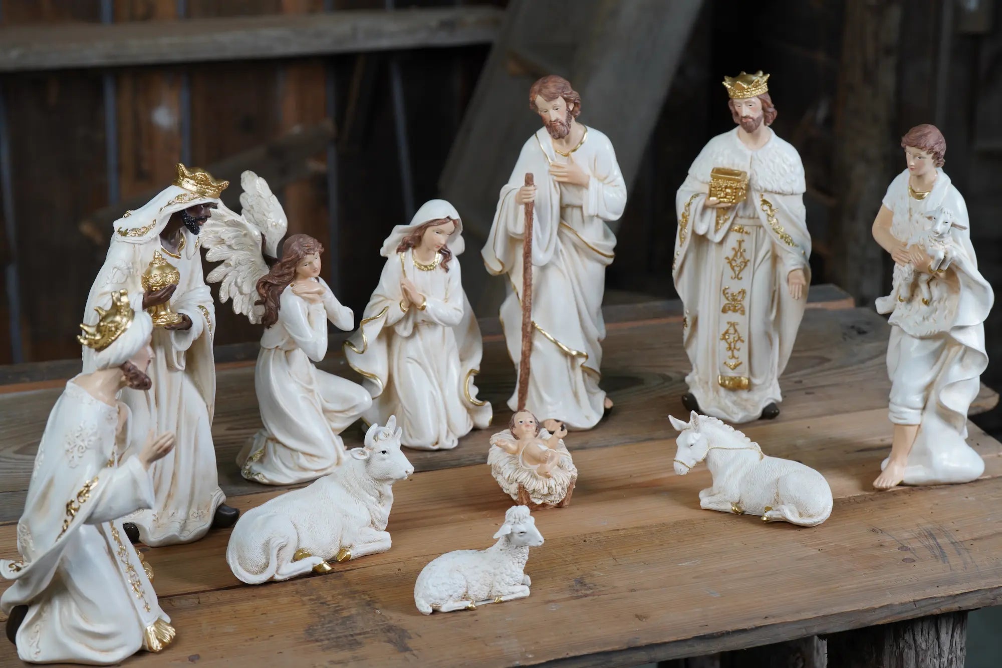 Complete white and gold 11-piece nativity scene displayed on rustic wood surface — all figures in ivory and gold finish