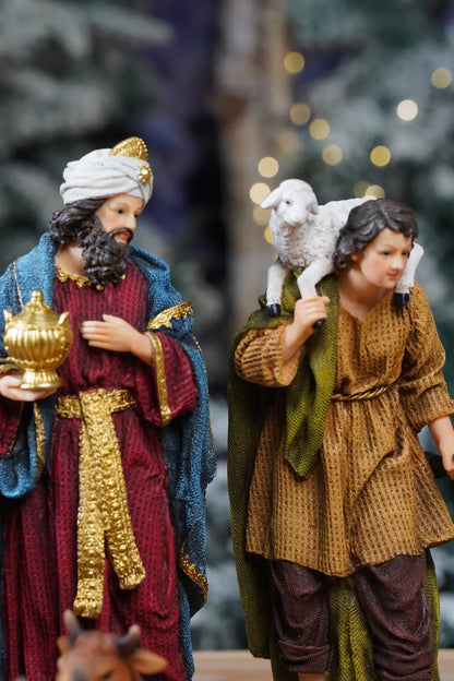 Wise Man in teal and crimson robe and young shepherd with lamb on shoulder — colorful nativity figurines close-up