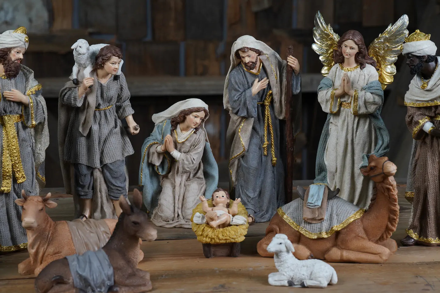 Grey and gold nativity scene displayed on rustic wood surface with Holy Family, angel, shepherd, Wise Men, and stable animals including camel