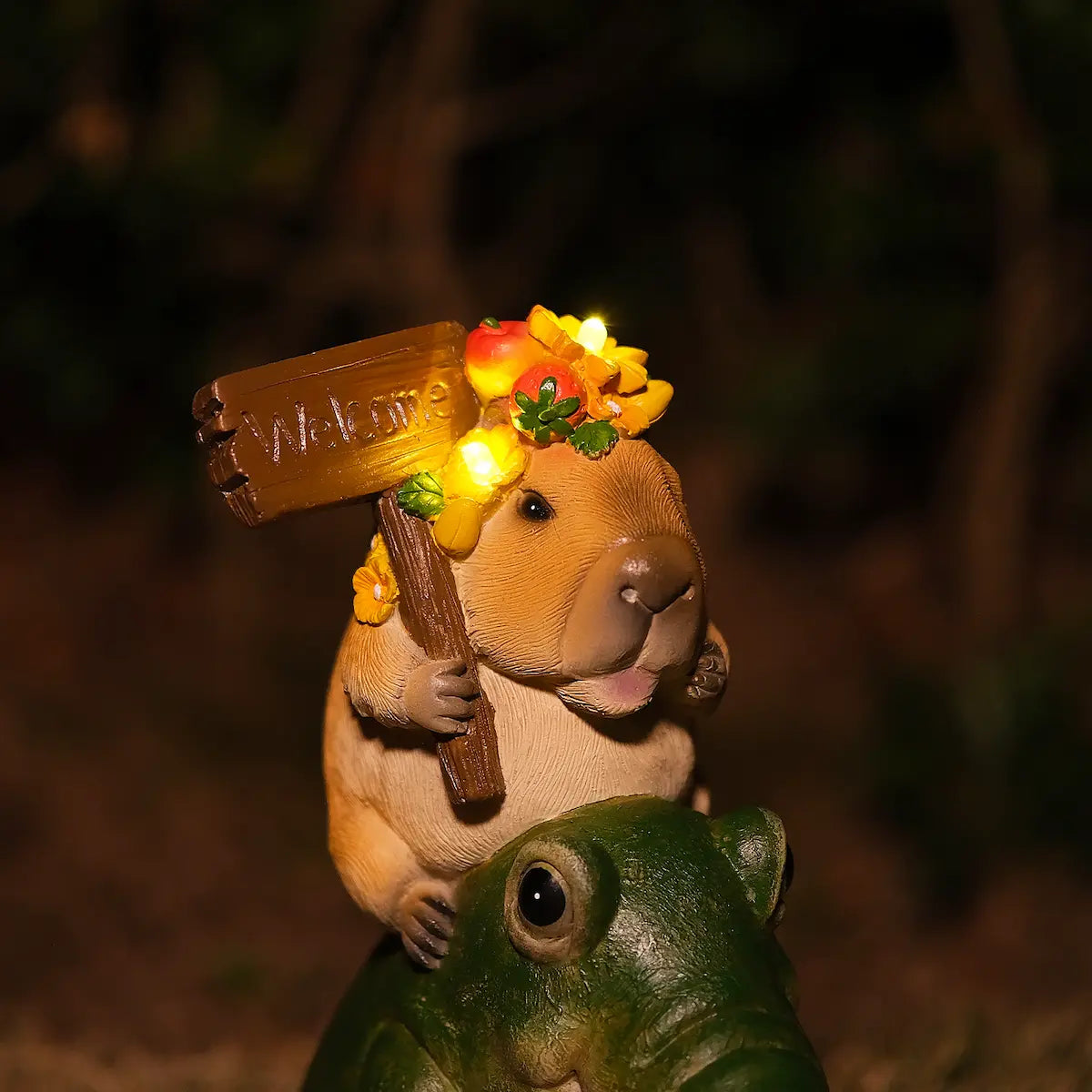 solar-powered lit capybara statue on alligator with glowing flowers and welcome sign in dark setting