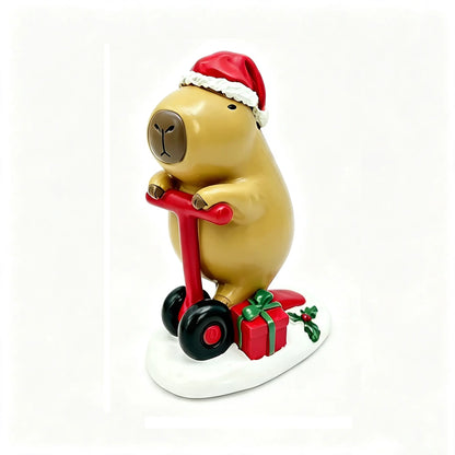 A Christmas capybara figurine wearing a red Santa hat and riding a red scooter, with a red gift box and green holly on a white base