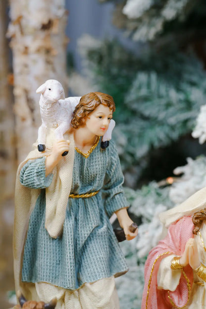 A shepherd figurine carrying a white lamb on his shoulders, wearing a textured blue tunic and cream pants.