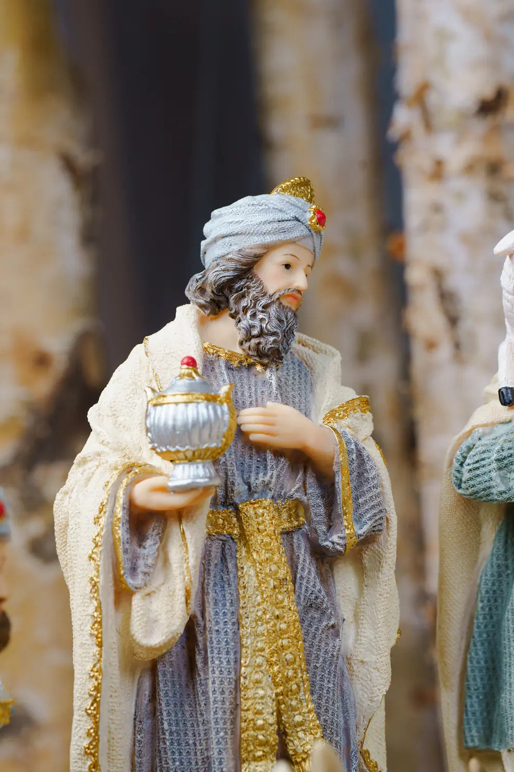 A figurine of a wise man in traditional robes, holding a silver goblet, set against a blurred background.