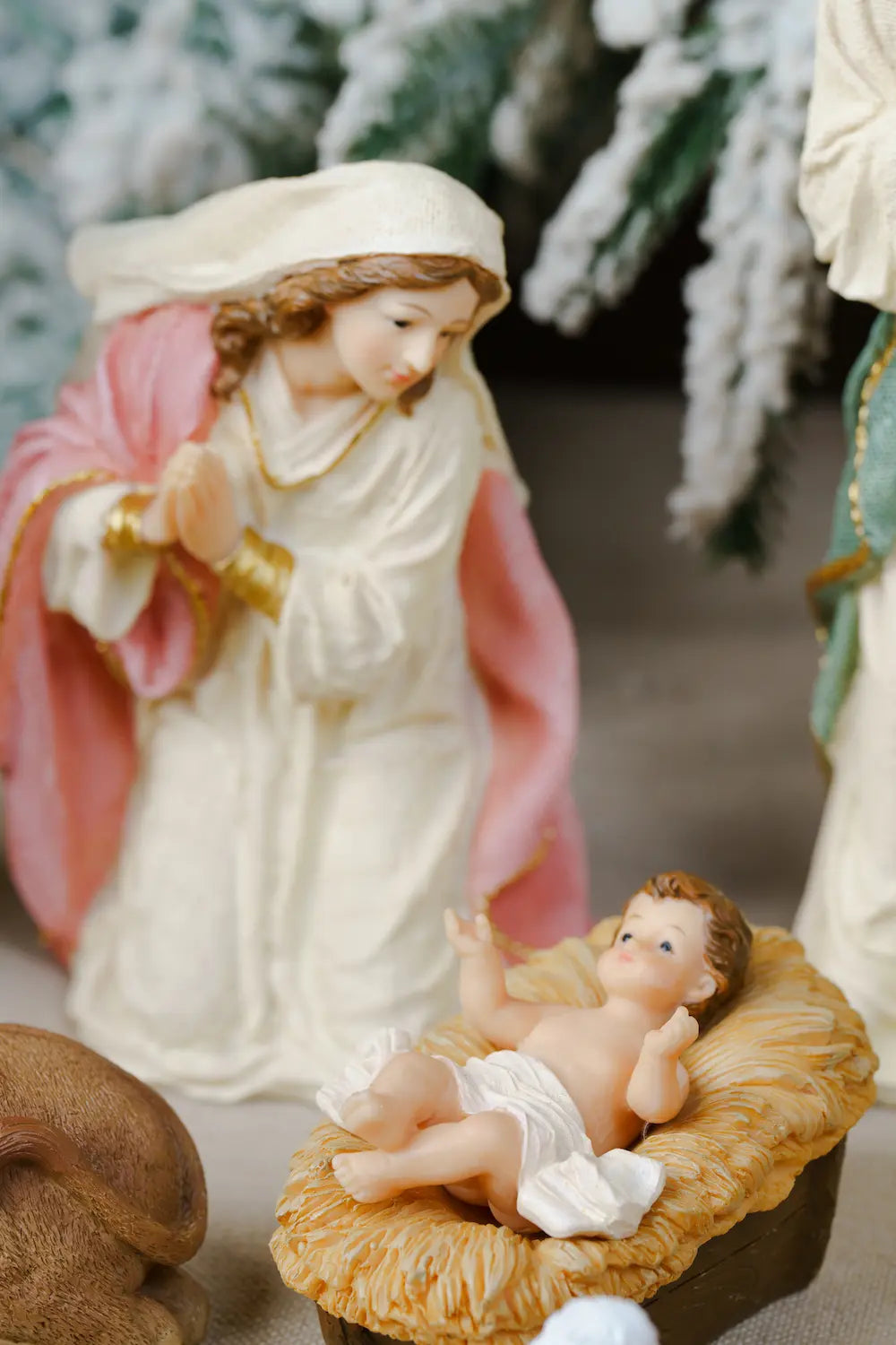 Christmas nativity scene figurine featuring Mary in cream robe, pink cloak, gold accents, gazes at baby Jesus in straw manger, close-up 