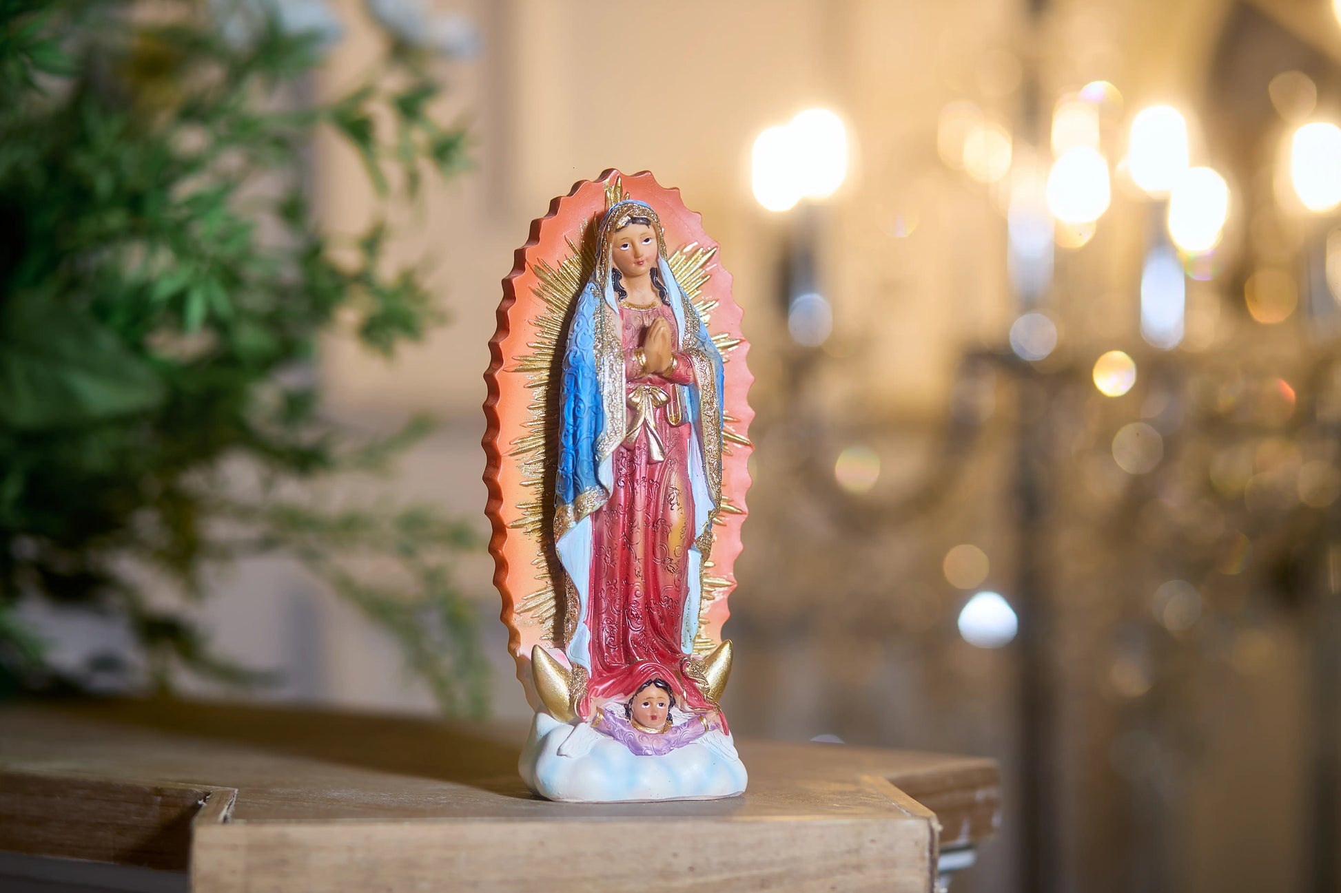 Religious Virgin Mary statue with golden rays displayed near greenery and candlelight