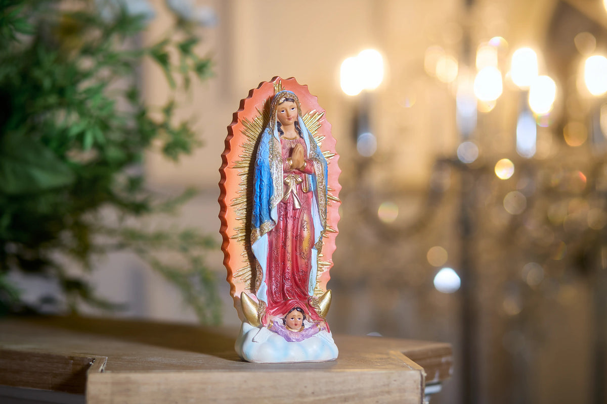 Religious Virgin Mary statue with golden rays displayed near greenery and candlelight