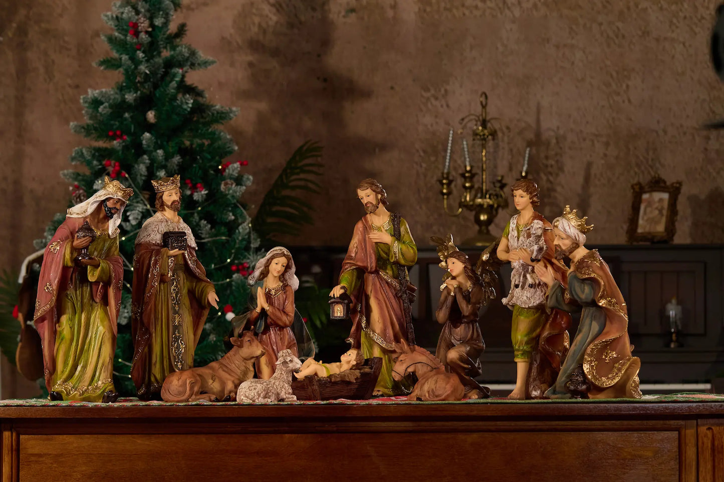 Complete nativity scene with kneeling angel displayed on sideboard in candlelit room with Christmas tree