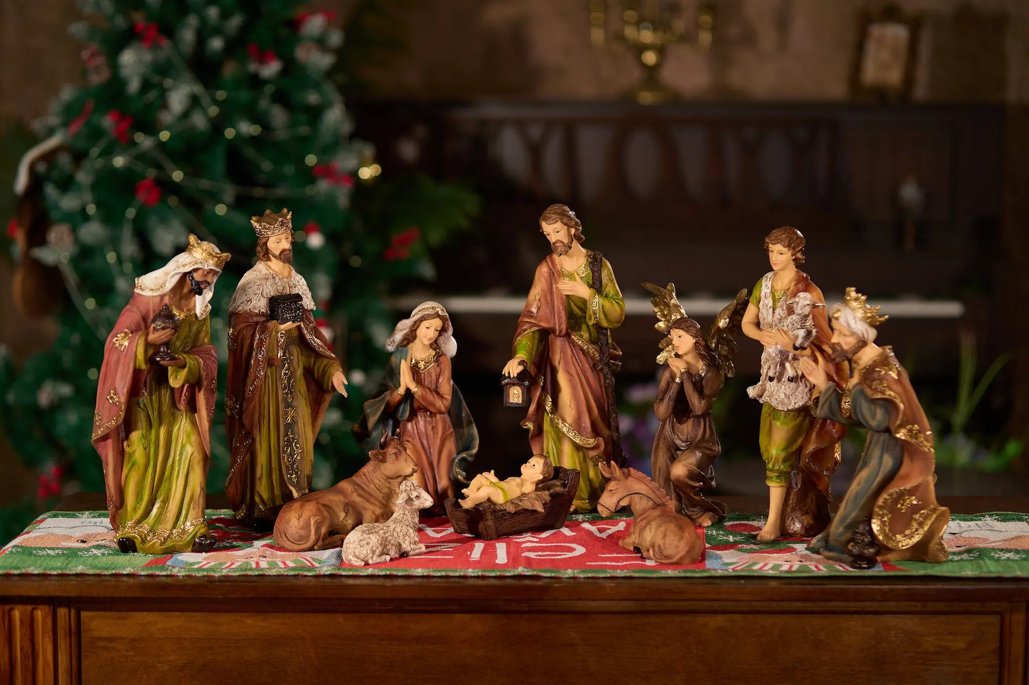 11-piece nativity figurine set on holiday Christmas table runner viewed from alternate angle in warm ambient light