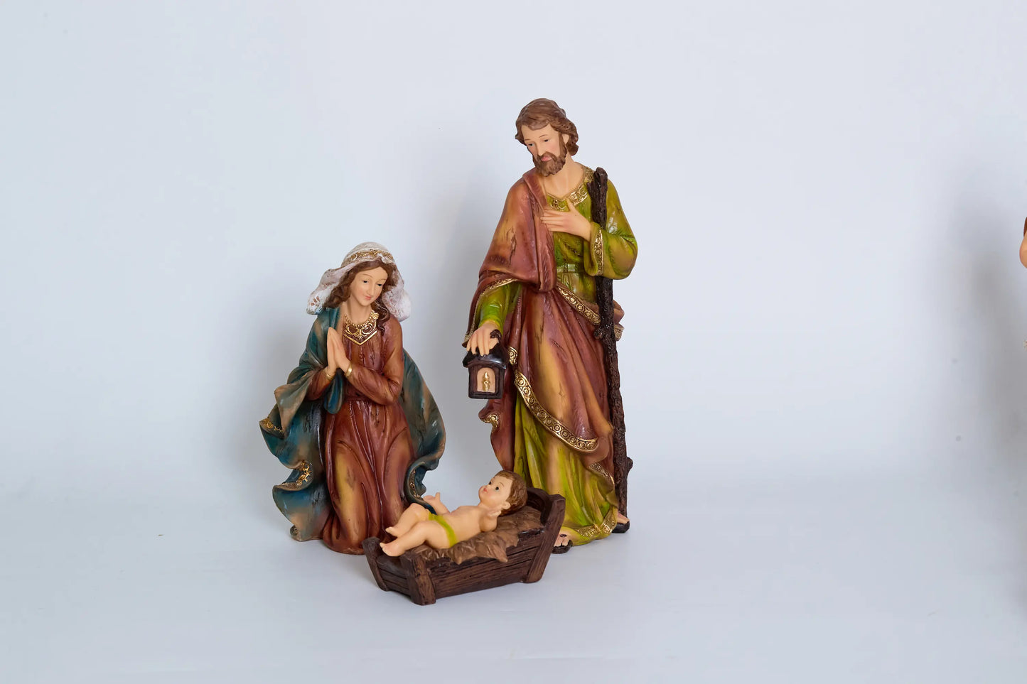 Holy Family close-up — kneeling Mary, Joseph with staff and lantern, and Baby Jesus in carved wooden cradle manger
