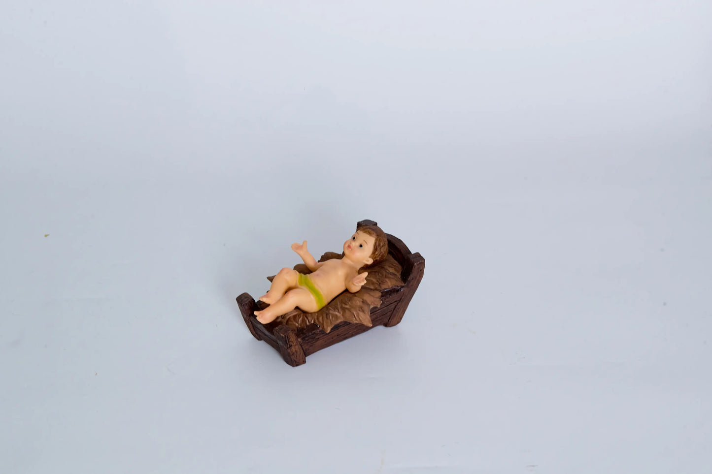 Baby Jesus nativity figurine close-up resting in carved wooden cradle manger — hand-painted resin crèche piece