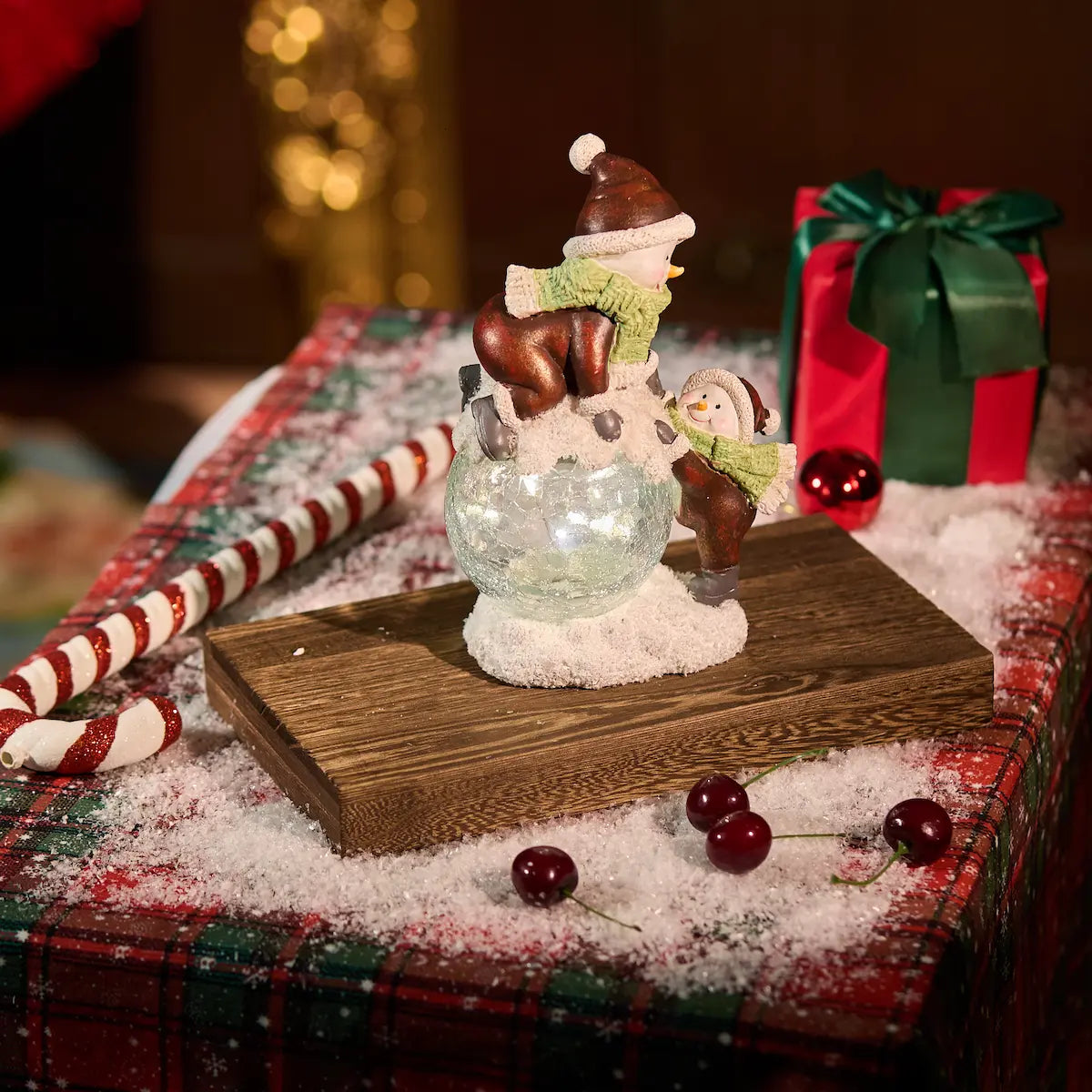 Lighted crackle-glass snowman figurine pair on wood block with candy canes and cherries — warm white LED Christmas tabletop decoration with holiday gift backdrop