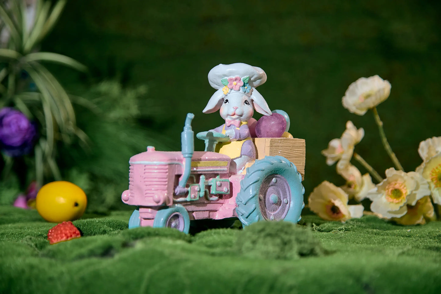Pastel Easter bunny chef tractor figurine on moss surface with spring flowers and Easter eggs — glitter resin farmhouse spring decoration