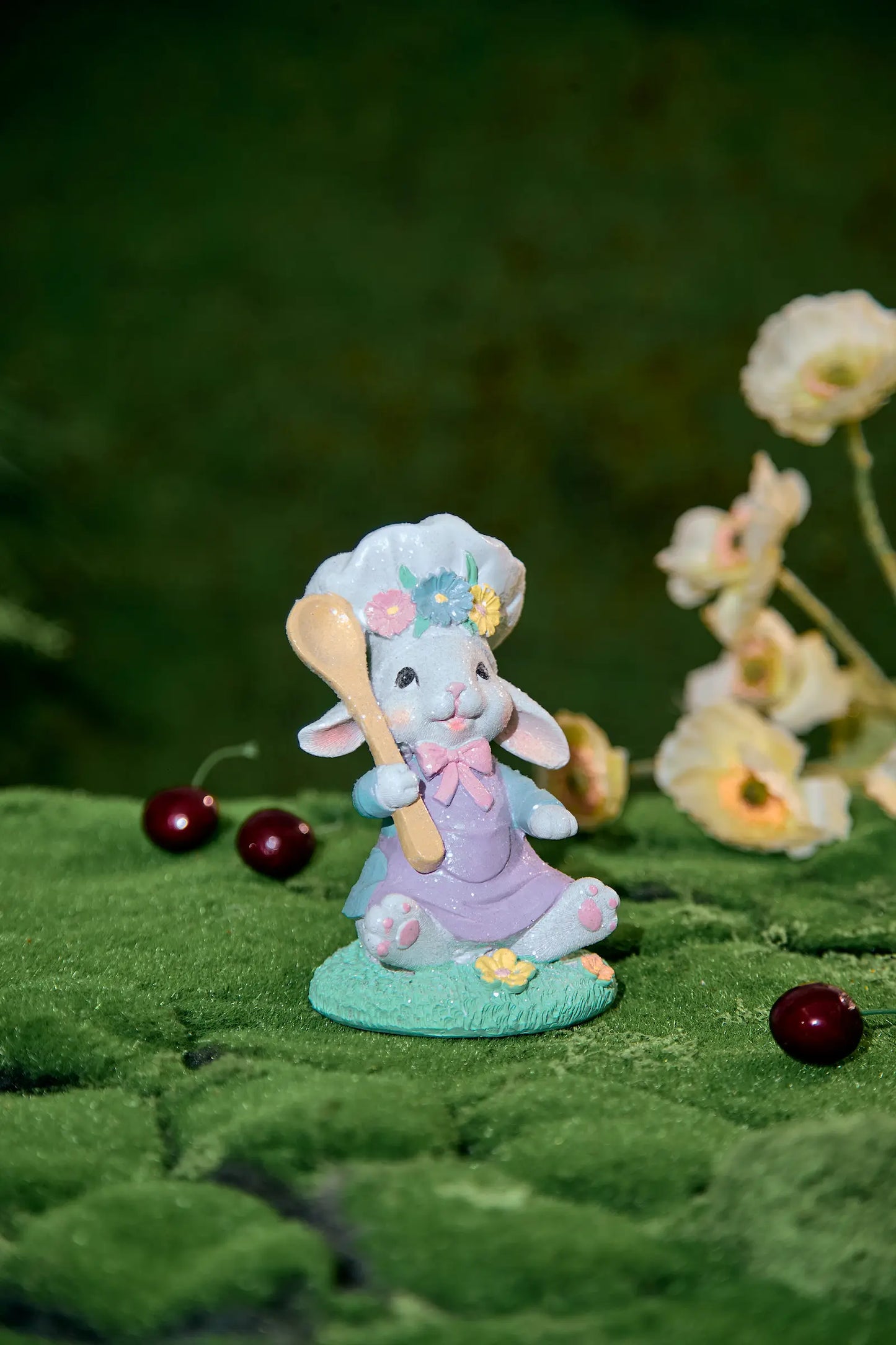 Easter bunny chef figurine with flower toque and golden spoon on moss with bokeh flower background — pastel resin spring tabletop accent