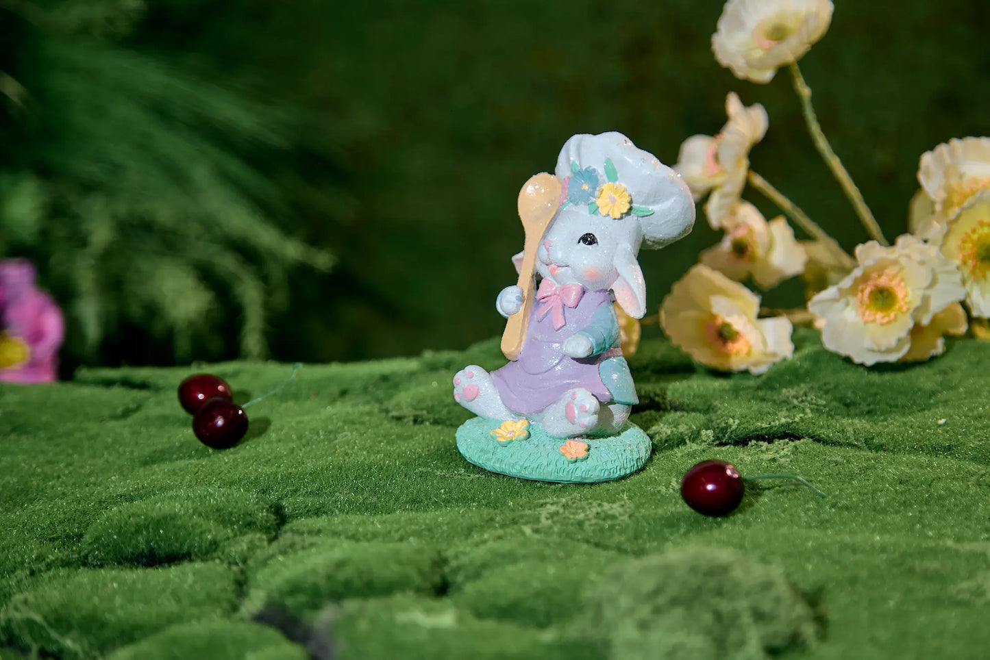 Side-angle Easter bunny chef figurine on moss surface with white spring flowers — hand-painted lavender and sky-blue glitter resin decoration