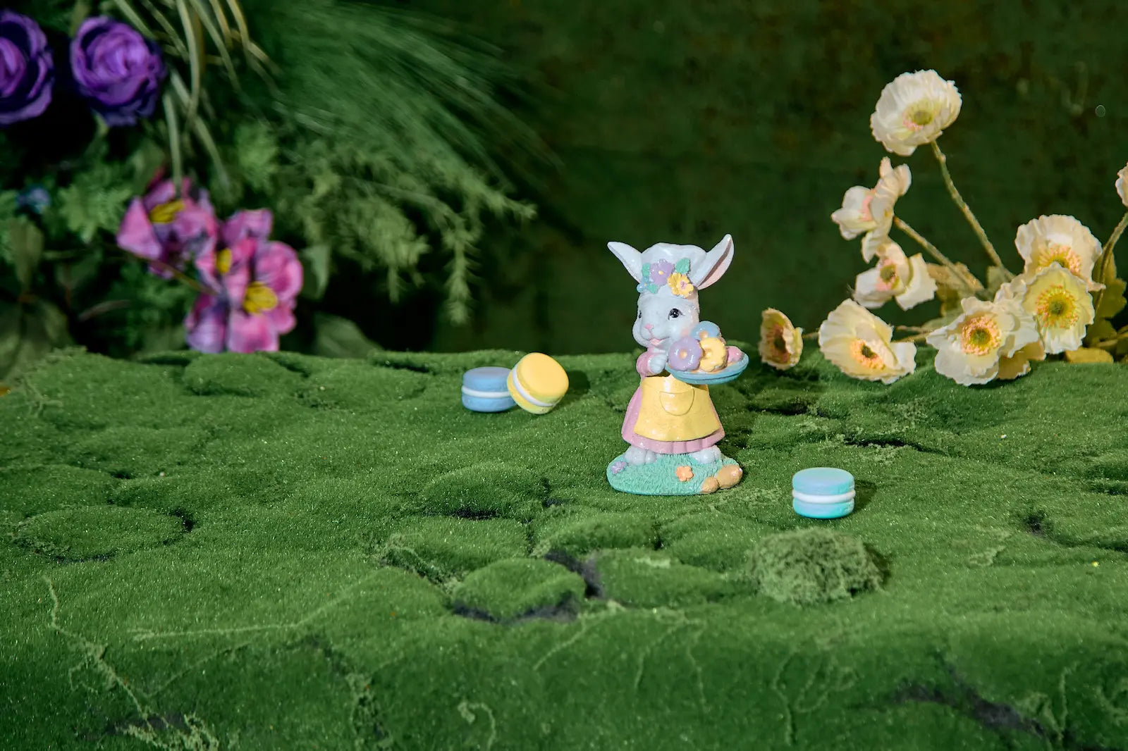 Small Easter bunny donut tray figurine on moss surface with macarons and spring flowers — pastel resin cottagecore spring décor wide shot