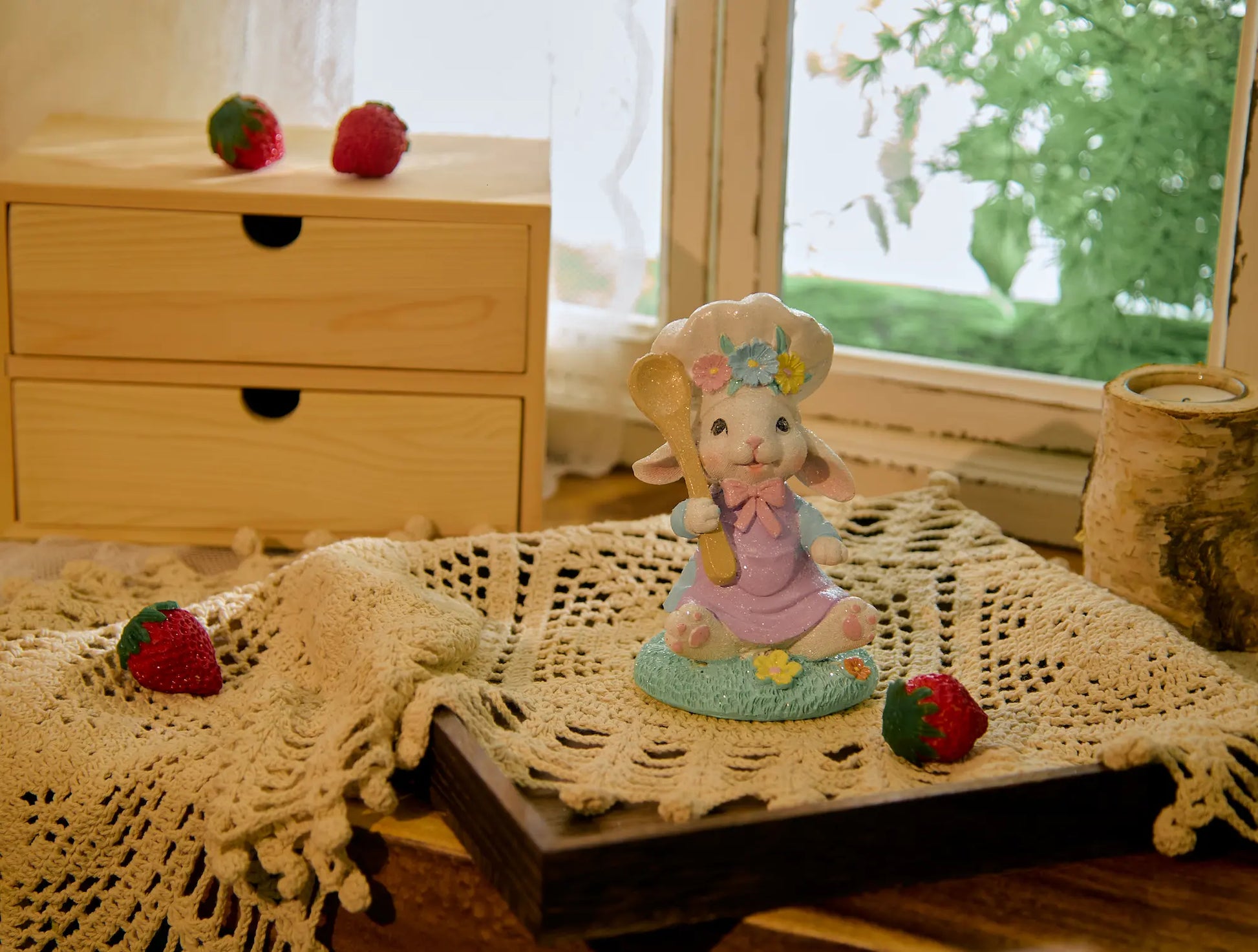 Easter bunny chef figurine centered on lace doily with wooden drawer unit and strawberries — cottagecore spring home decoration in window setting