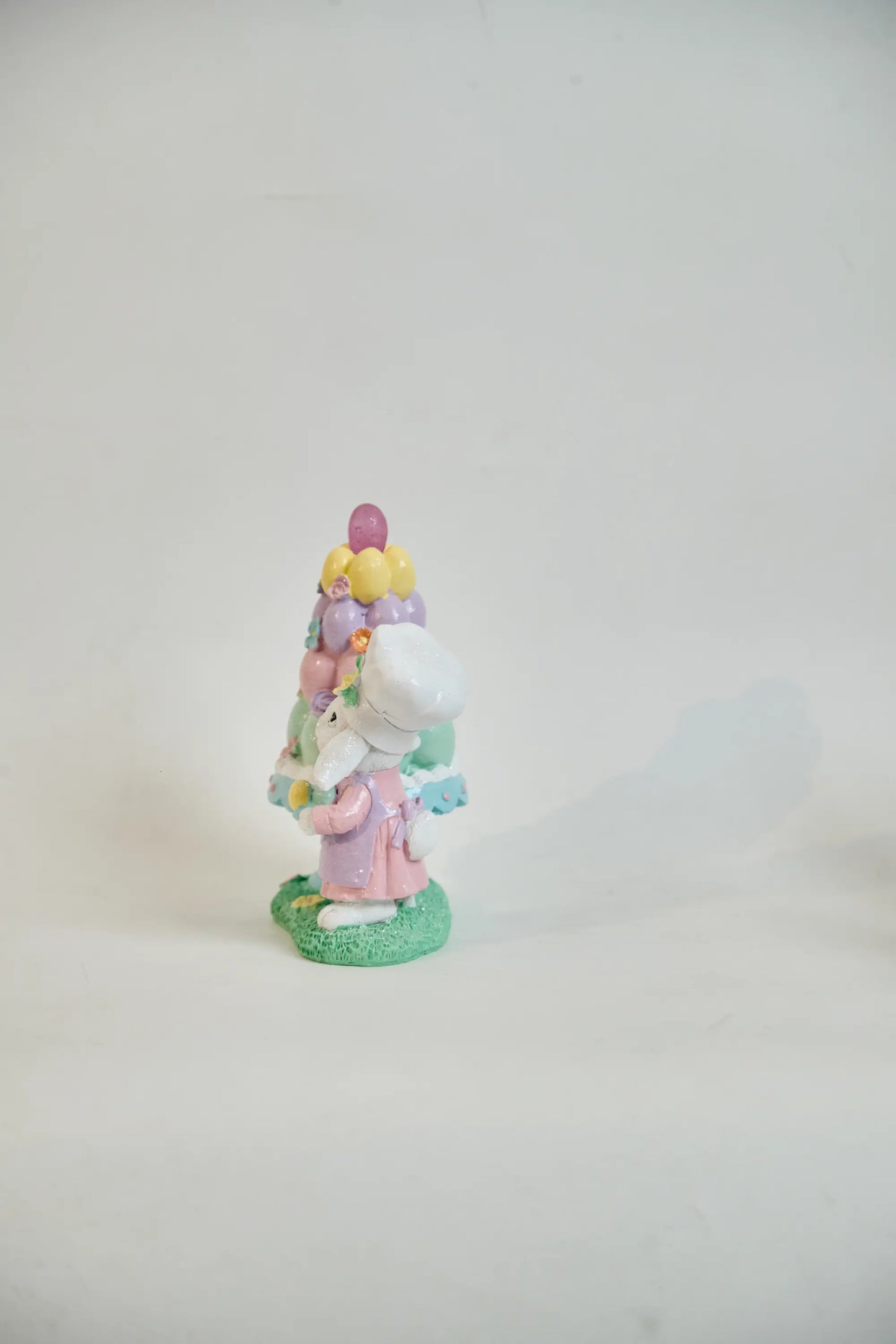Side view of Easter bunny baker figurine showing chef toque, lavender apron, and egg bowl detail — hand-painted glitter resin spring decoration
