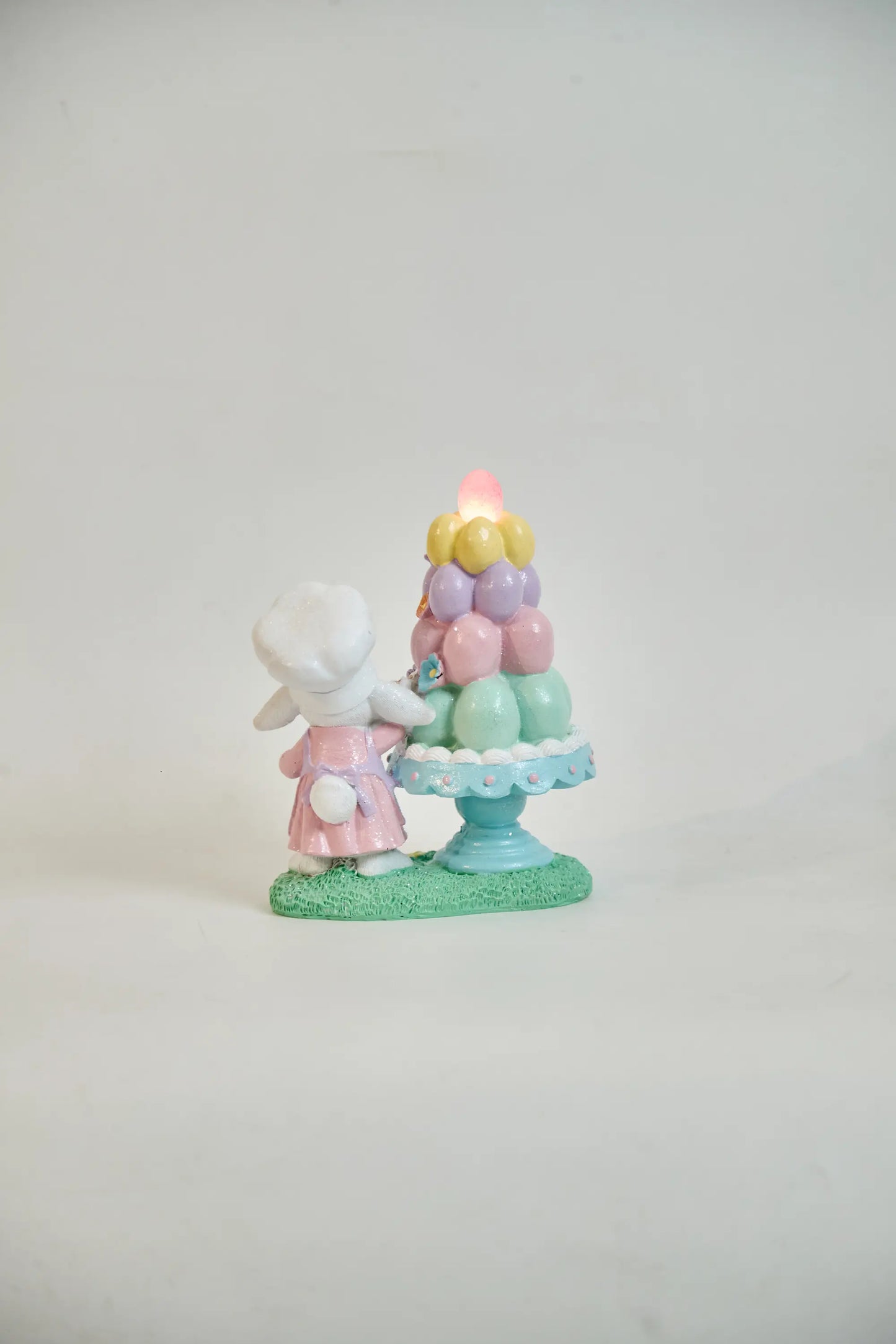 Rear view of lighted Easter bunny figurine showing glowing pink egg and scallop cake stand edge detail — battery LED glitter resin spring décor