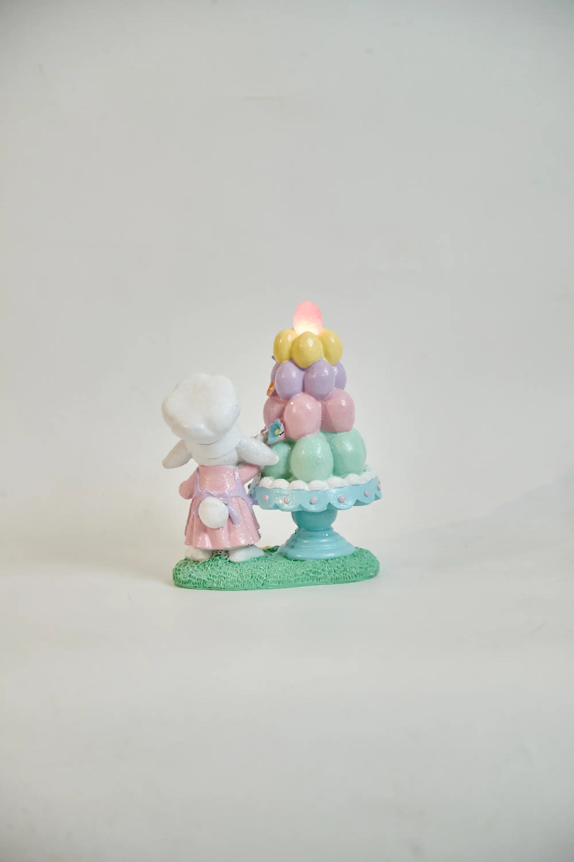 Rear view of lighted Easter bunny figurine showing glowing pink egg and scallop cake stand edge detail — battery LED glitter resin spring décor