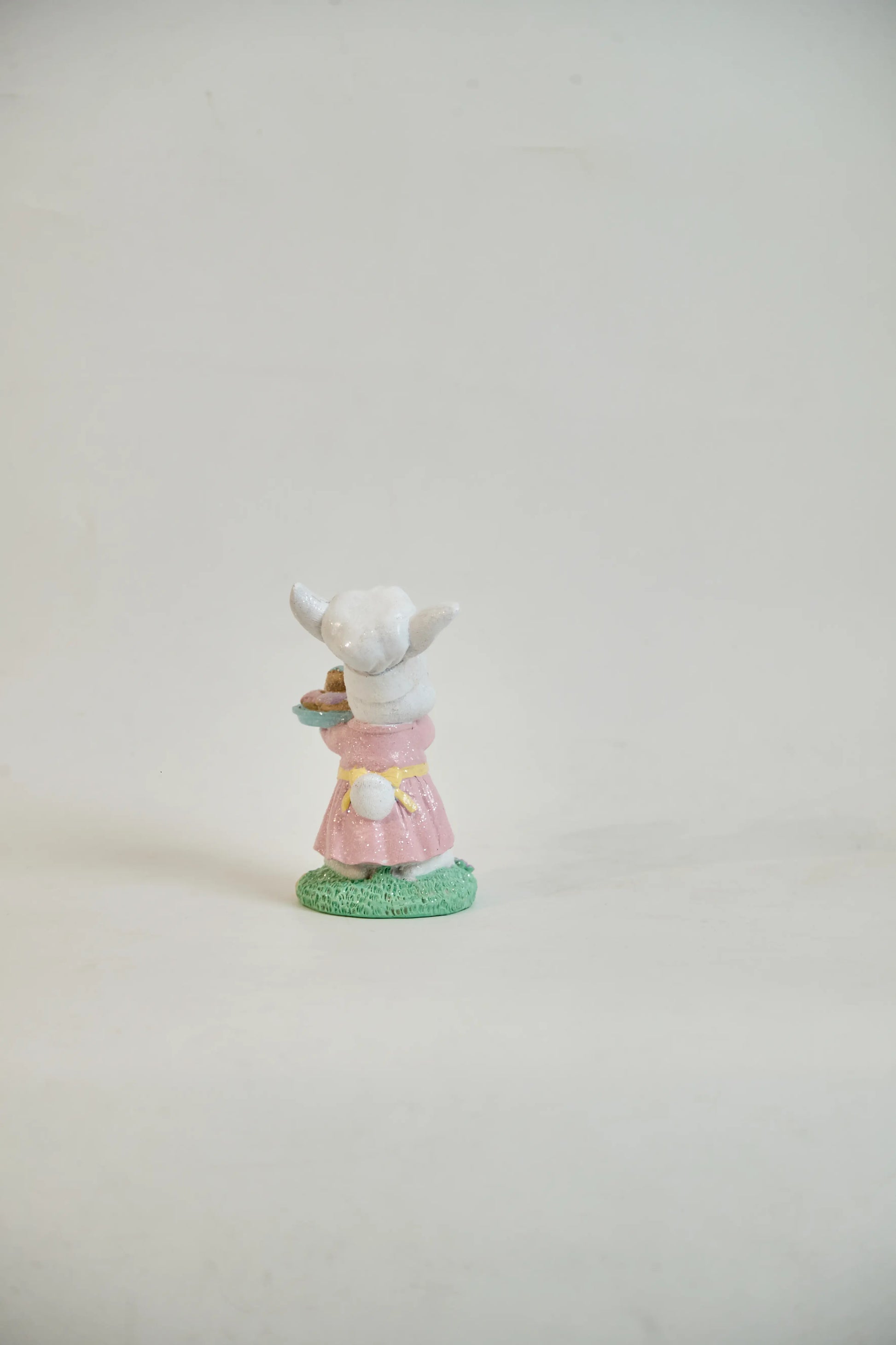 Rear view of Easter bunny figurine showing white cotton tail, yellow sash, and pink ruffled hem — glitter resin spring tabletop accent