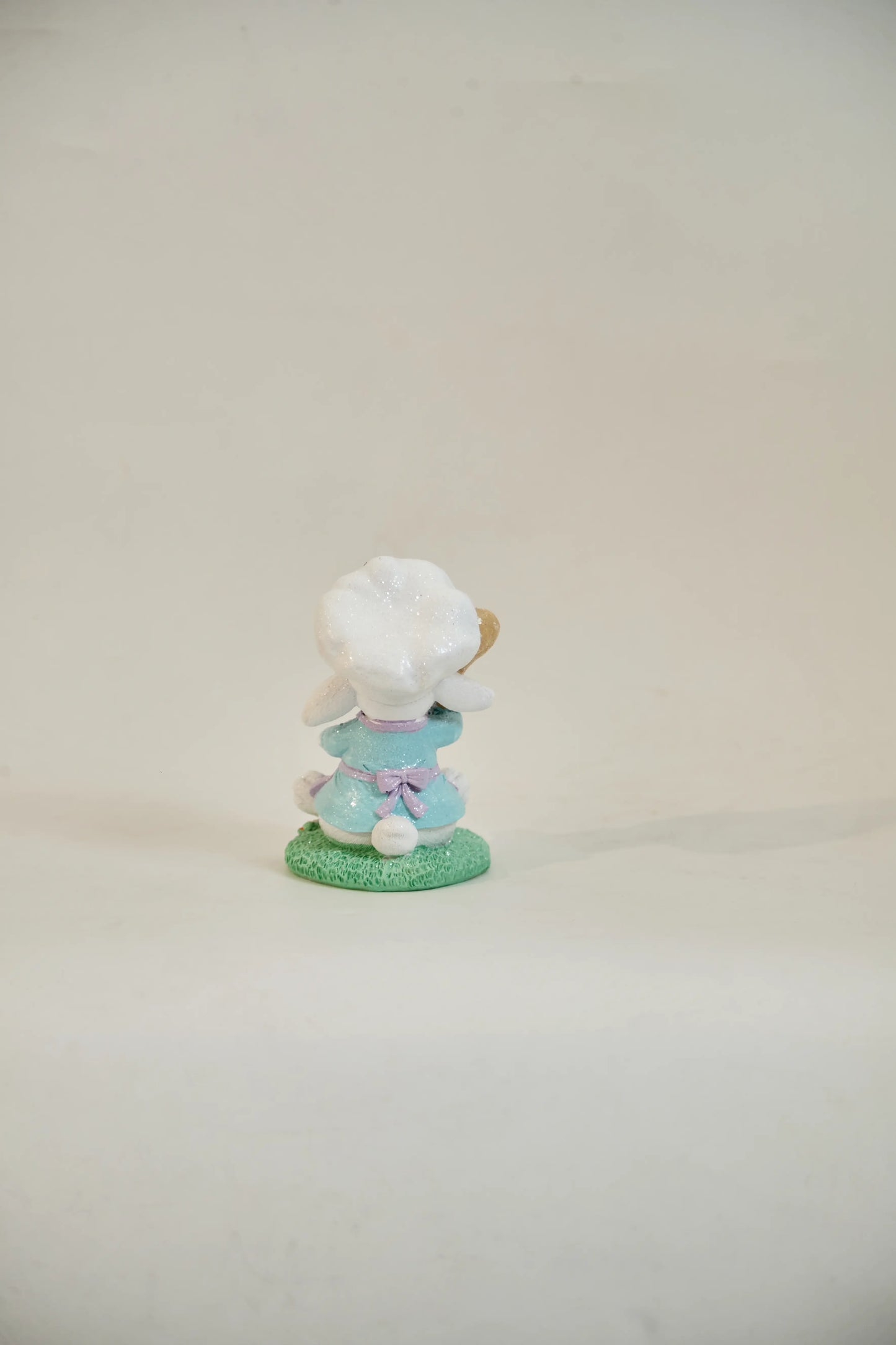 Rear view of Easter bunny chef figurine showing lavender apron bow, sky-blue outfit, and white cotton tail — glitter resin spring tabletop accent