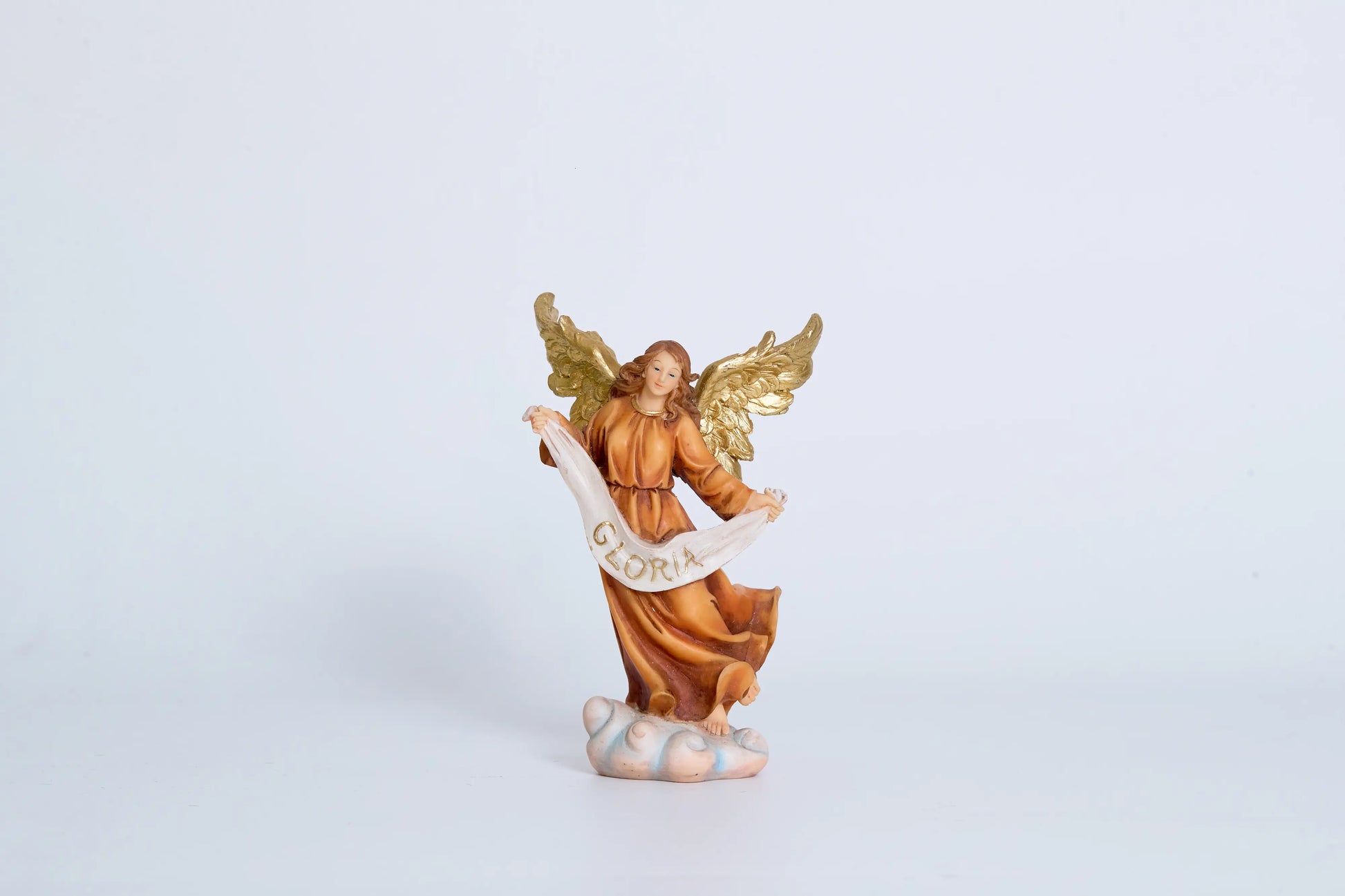 Herald angel nativity figurine close-up — Gloria banner angel with spread gold wings and flowing amber robe standing on cloud pedestal, hand-painted resin