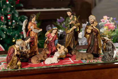 Nativity scene displayed on festive runner with Christmas tree lights, indoor tabletop holiday centerpiece.