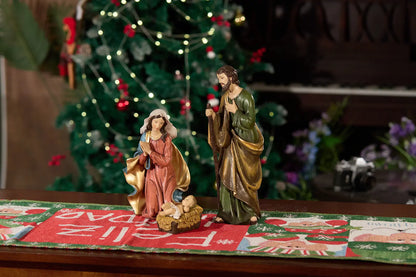Mary and Joseph nativity figurines beside manger on Christmas table runner — hand-painted resin Holy Family