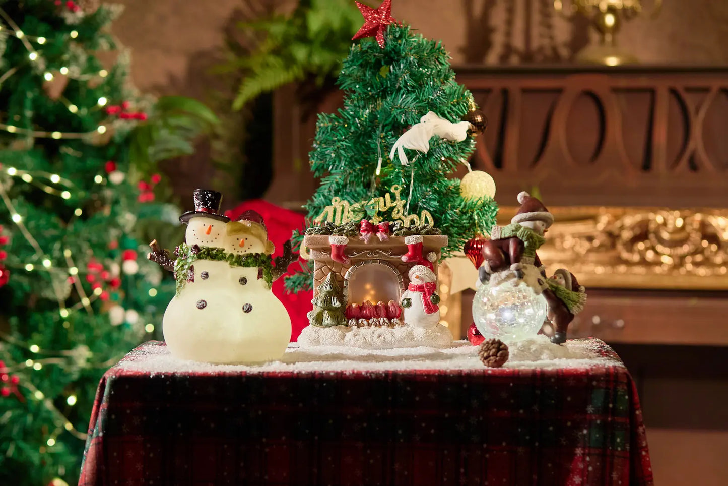 Zayton snowman couple figurine displayed with crackle-glass snowman and lighted fireplace figurine — Christmas snowman decoration collection on plaid surface