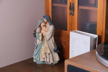 Holy Family statue displayed on wood shelf beside glass cabinet and notebook — Mary, Joseph, and Baby Jesus figurine home decor