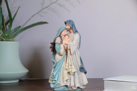 Holy Family statue on tabletop beside potted plant and books — hand-painted resin Mary and Joseph figurine with Baby Jesus
