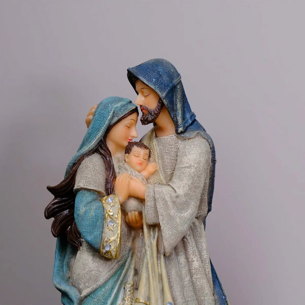 Holy Family statue close-up — Mary and Joseph foreheads touching over swaddled Baby Jesus, hand-painted resin devotional figurine