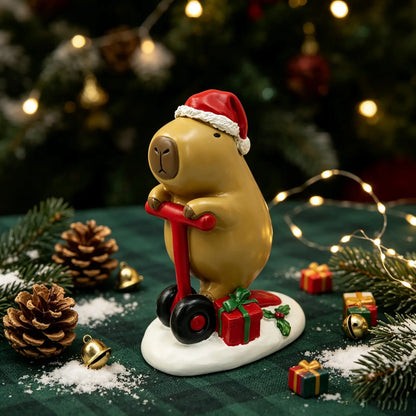 the capybara on scooter figurine displayed on a green surface with pine cones, gold bells, fairy lights, and mini gift boxes