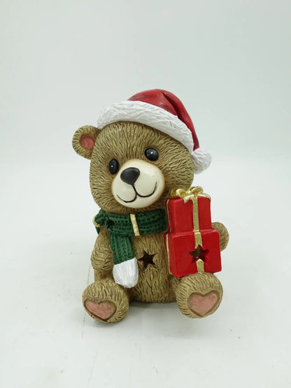 A Christmas teddy bear figurine holding a red gift box with gold ribbon, photographed against a plain light background.